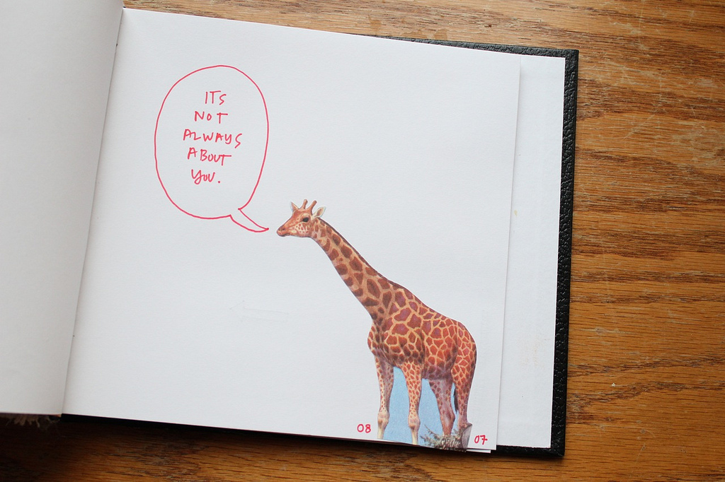 A journal page with a giraffe on it, with a handwritten speech bubble containing the words, "It's Not Always About You"