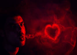 A mostly dark black image with a man in red blowing a red smoke heart. Looks a bit disturbing.