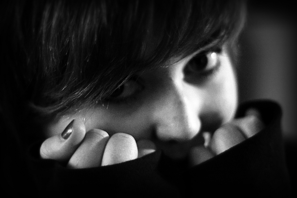 Black and white image of a young person hiding behind their hands.