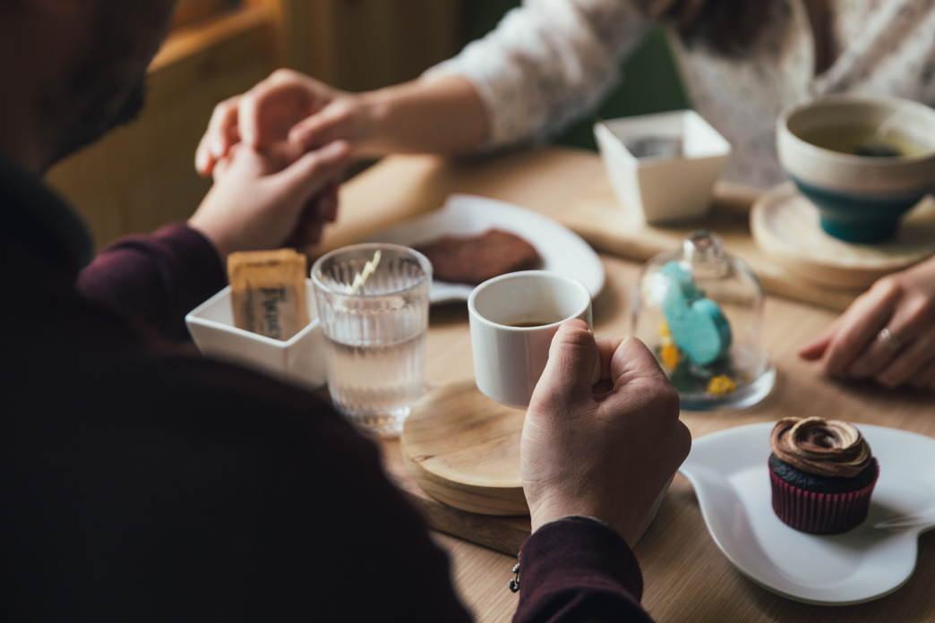 An man and a woman holdinghands across a table filled with coffee, cupcakes and soup.